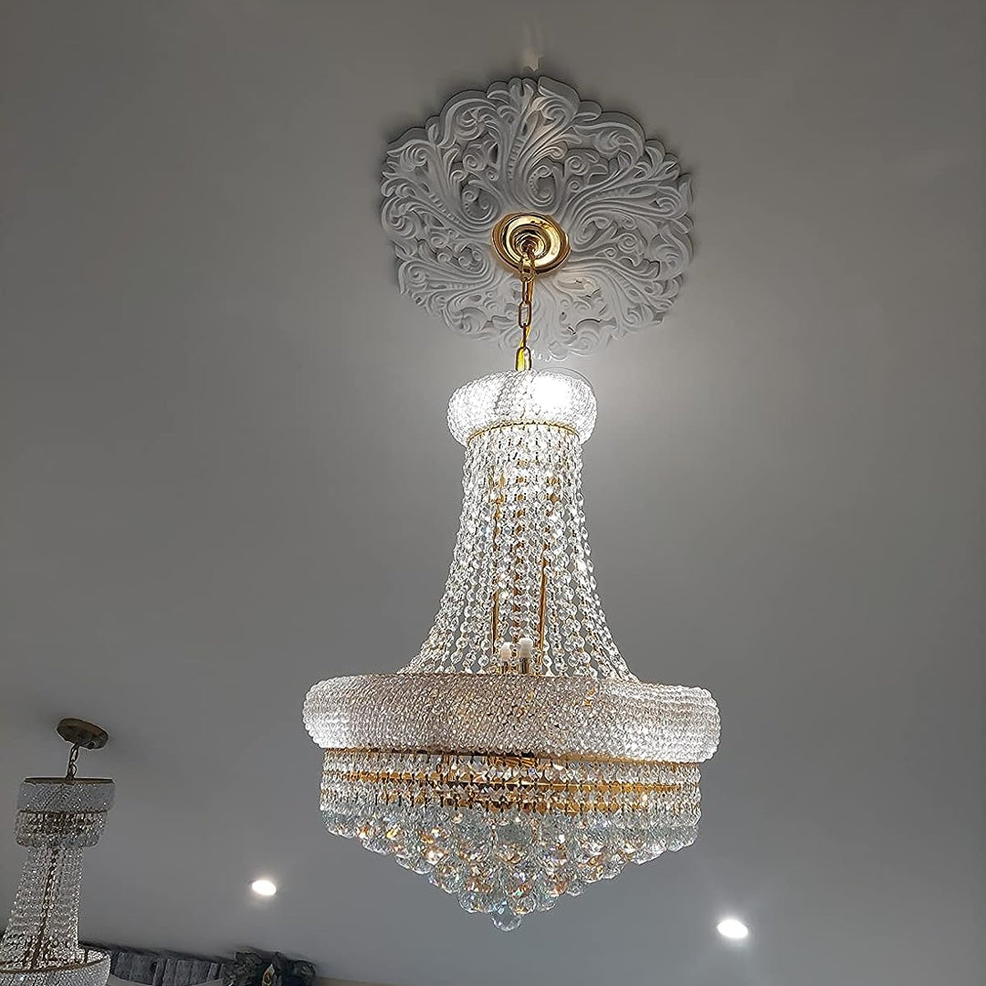 Crystal chandelier hanging from a decorative ceiling fixture against a plain wall.