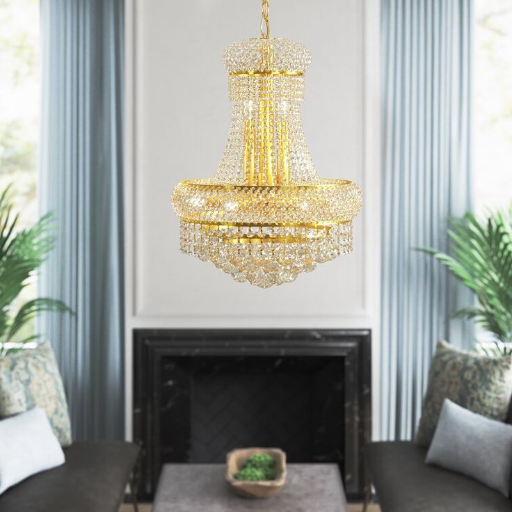 Gold chandelier hanging above a fireplace in a room with plants and furniture.