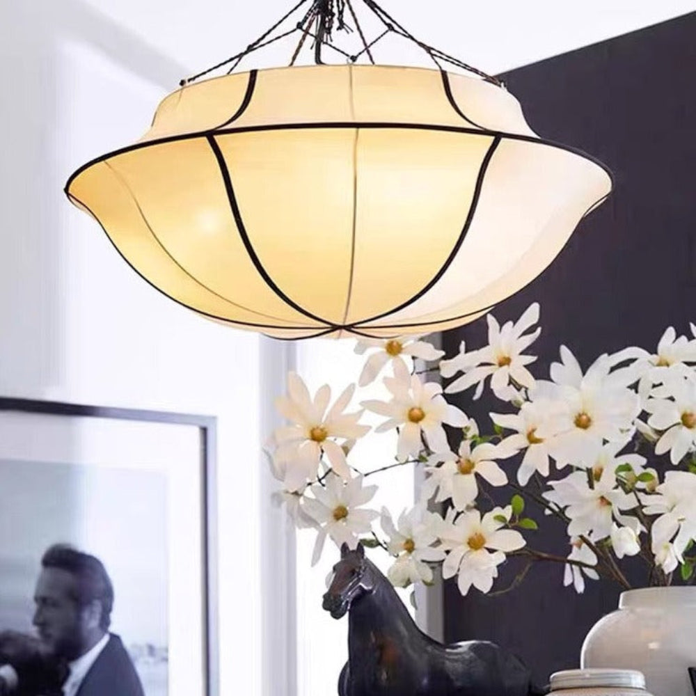 Decorative lampshade hanging above a table with books, a horse figurine, and flowers.