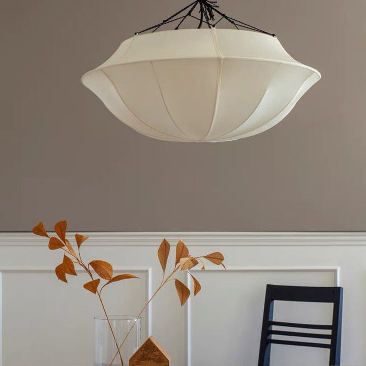Ceiling light fixture above a table with a vase and leaves on a neutral background