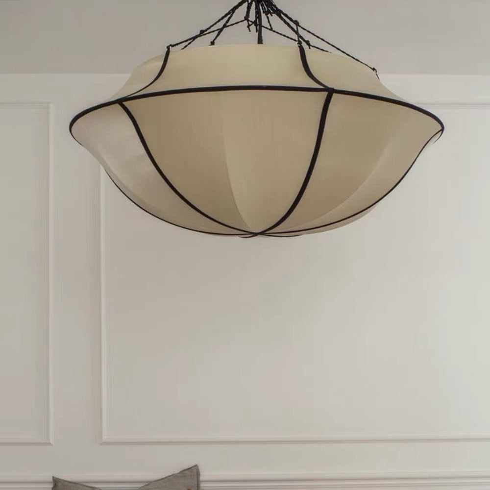 Beige ceiling light fixture above a bed with colorful pillows on a white wall.