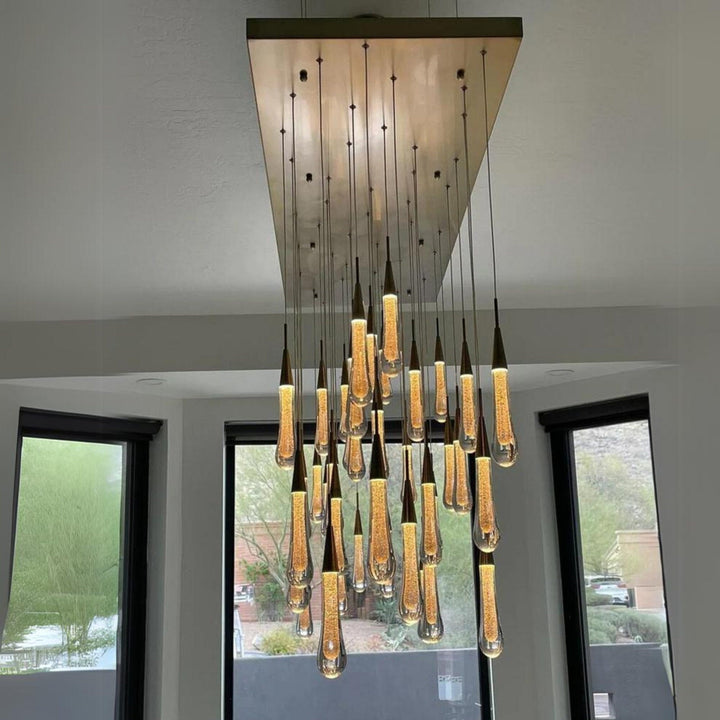 Modern chandelier hanging from a ceiling with large windows in the background