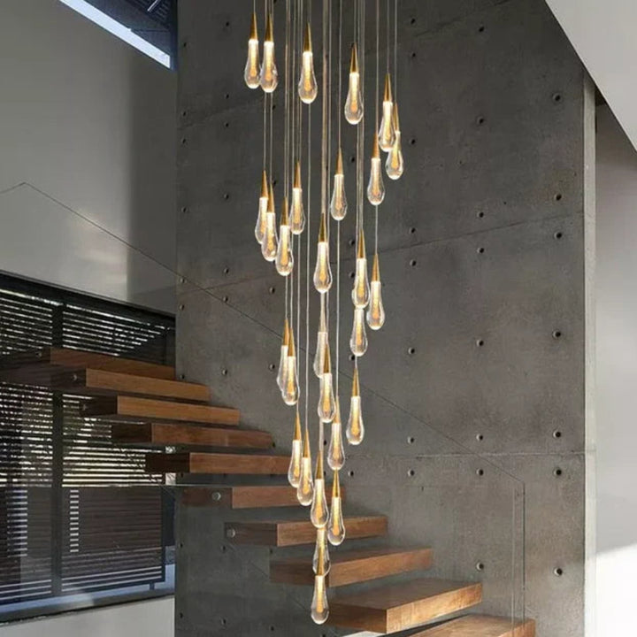 Modern chandelier with hanging light bulbs in a room with concrete walls and wooden stairs.