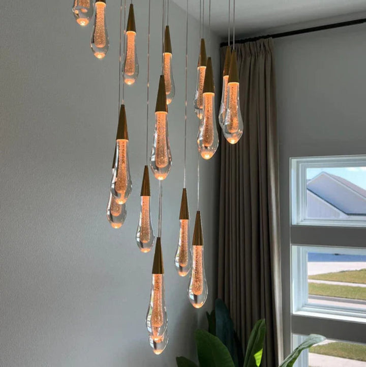 Modern chandelier with hanging light bulbs in a room with a window and curtains.
