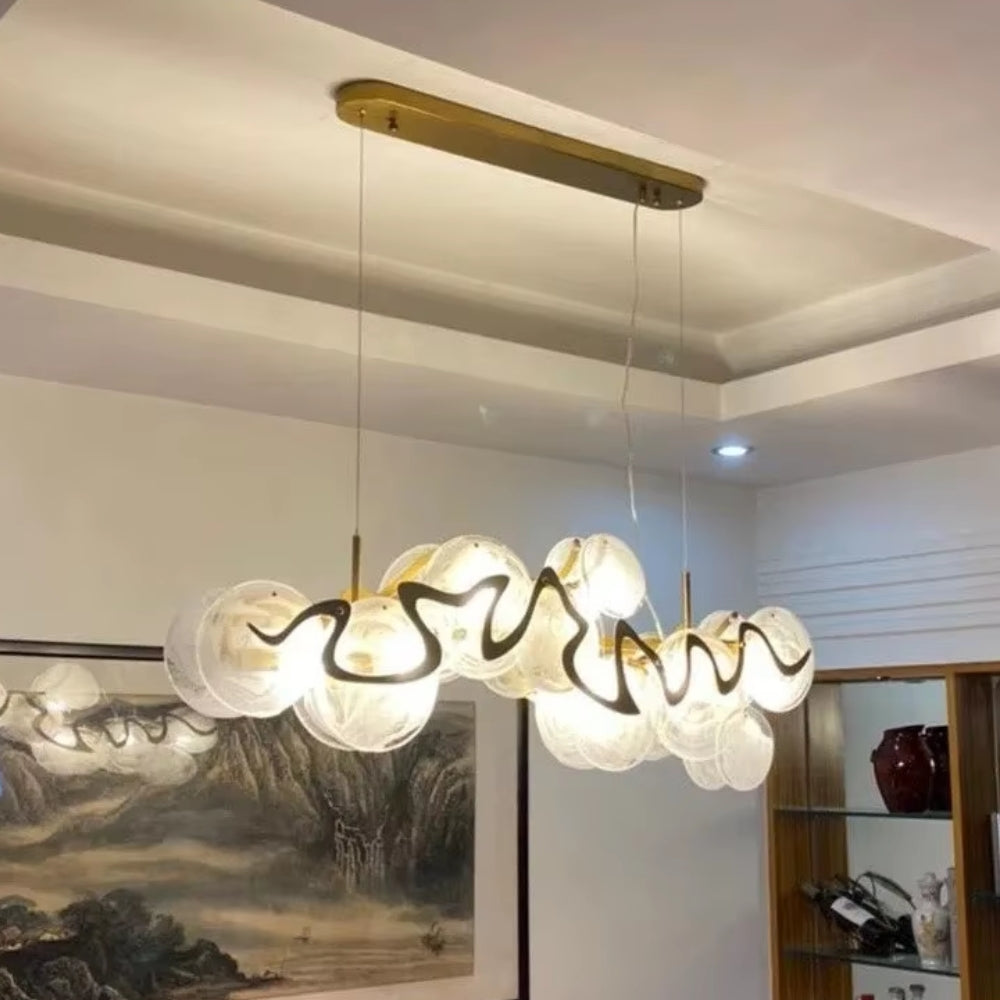 Modern chandelier hanging in a room with a painting and shelves in the background