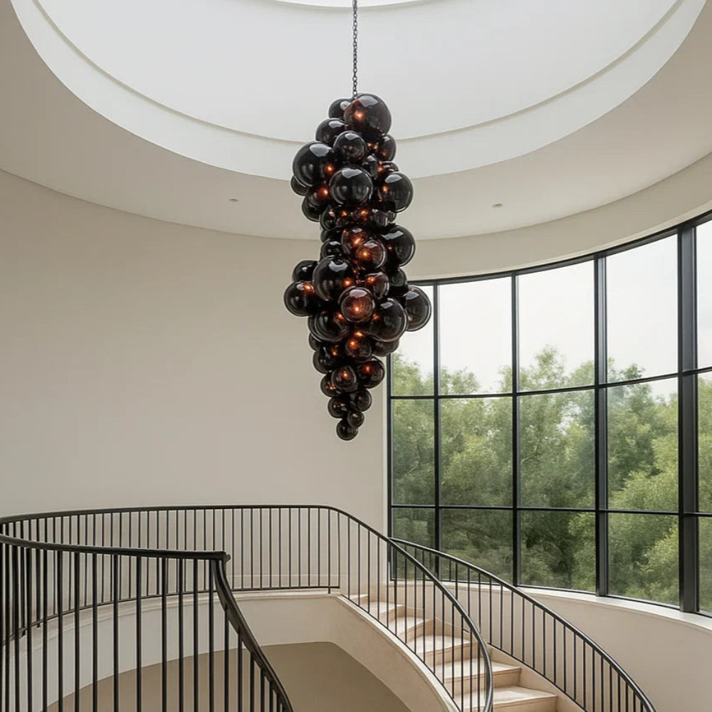 Modern staircase with a unique black chandelier in a well-lit room with large windows.