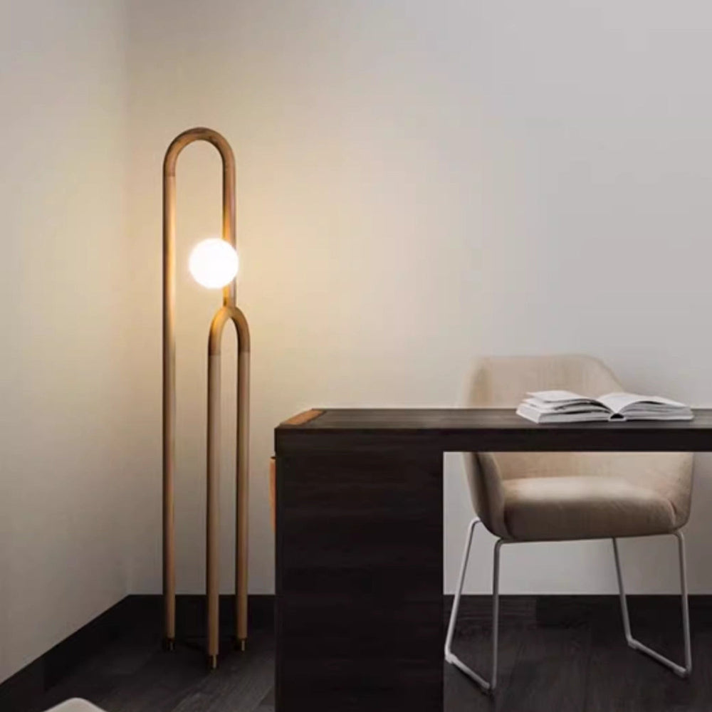 Modern floor lamp next to a desk with a chair in a minimalistic room.