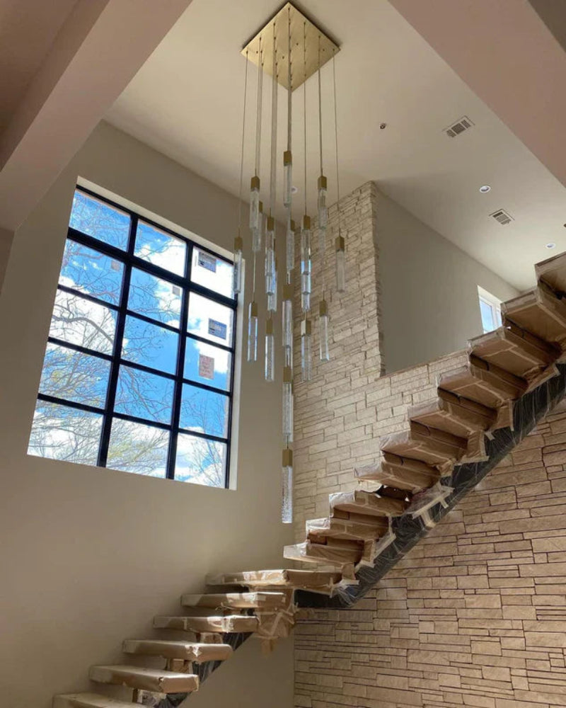 Modern staircase with Squatu chandelier in a well-lit room with large windows.