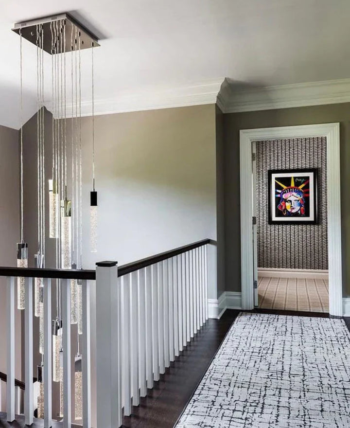 Modern staircase with glass balustrade and decorative light fixture, leading to a room with abstract art on the wall.