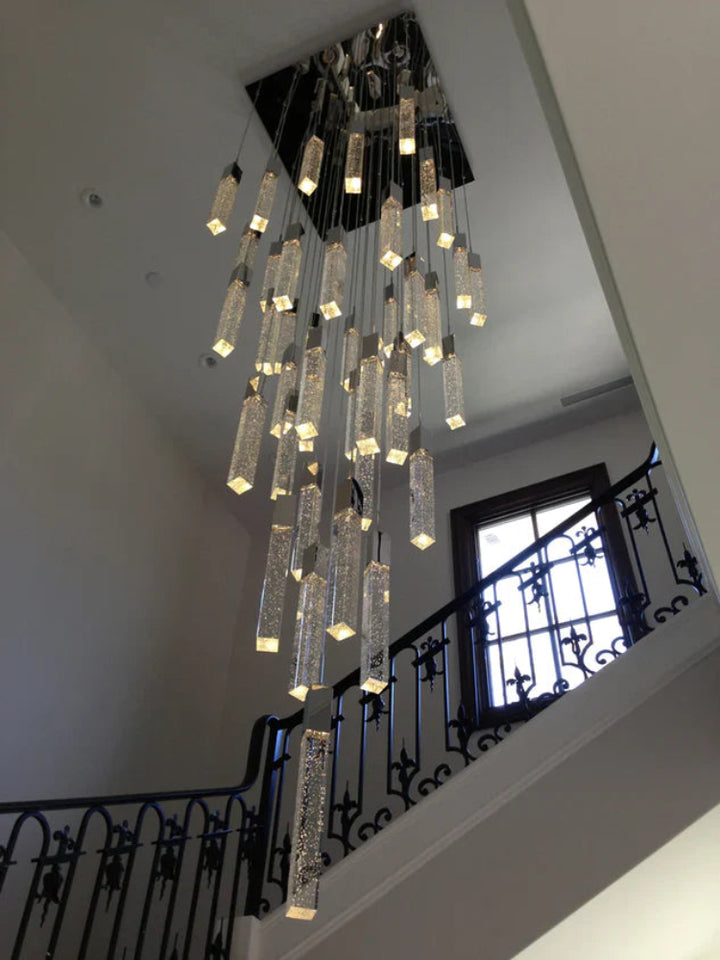 Crystal chandelier hanging in a staircase area with white walls and black railings.
