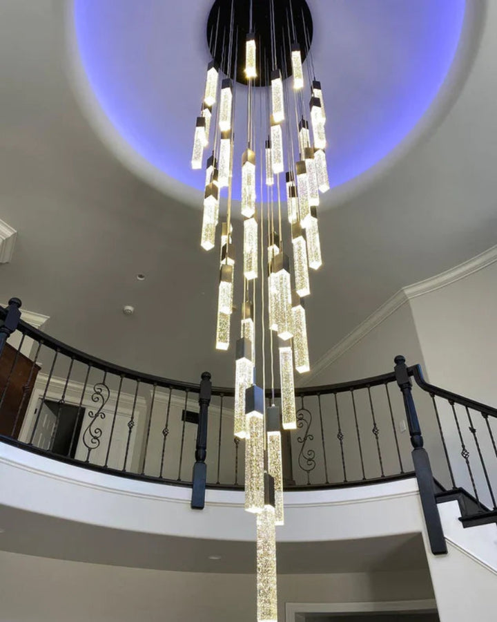Chandelier hanging from a ceiling in a home with a staircase in the background. SQUATU Crystsal Pendant Lighting